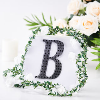 Black letter "B" surrounded by greenery and white flowers.