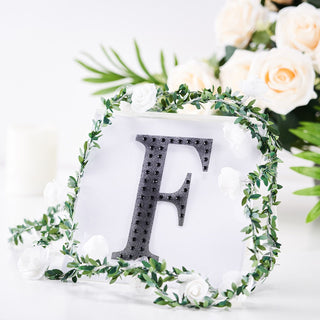 Decorative letter F surrounded by greenery and flowers on a white background.