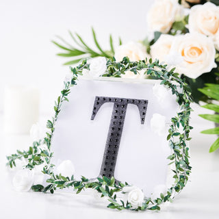Decorative letter "T" with floral accents and greenery.