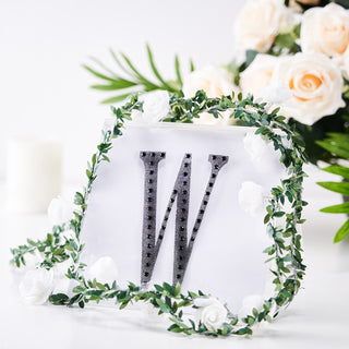 Decorative letter "W" surrounded by greenery and flowers.