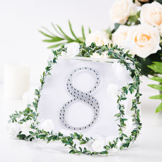 Clear acrylic table number 8 surrounded by greenery and white flowers.