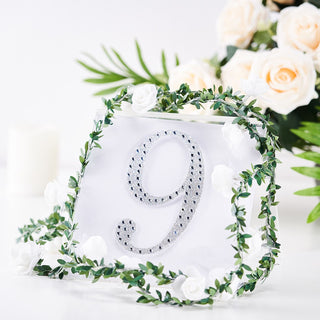Decorative table number 9 with rhinestones, surrounded by greenery and white roses.