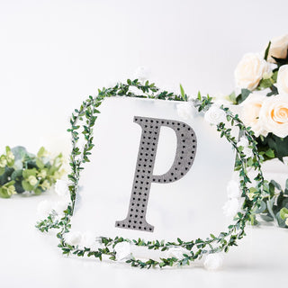Decorative letter "P" with rhinestones surrounded by floral greenery.