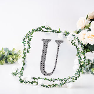 Decorative letter U surrounded by greenery and flowers.