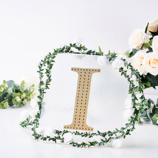Gold letter "I" surrounded by greenery and white flowers on a clear backdrop.