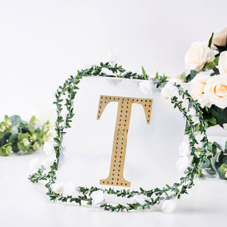 Gold letter "T" decor surrounded by floral accents on a clear backdrop.