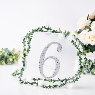 Table number sign with rhinestone '6' and floral greenery decoration.