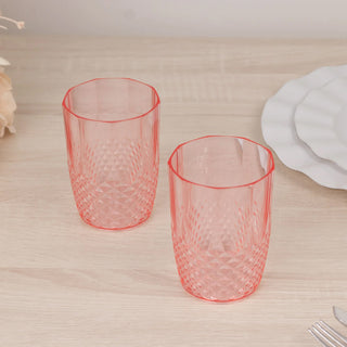 Two pink textured drinking glasses on a wooden surface.