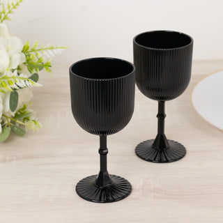 Black ribbed glass goblets on a wooden table with greenery