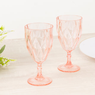 Pink crystal goblet glasses set on a wooden table with floral accents.
