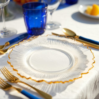 Elegant clear glass plate with gold rim on a beautifully set dining table.
