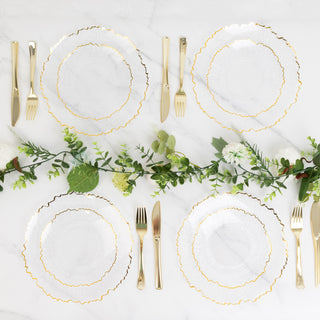 Elegant gold-rimmed plates set on a marble table with greenery and cutlery.