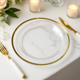 Clear glass plate with gold rim set on a marble table, accompanied by gold cutlery.