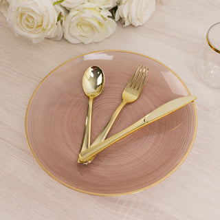 Elegant gold cutlery on a pink plate with subtle concentric patterns.