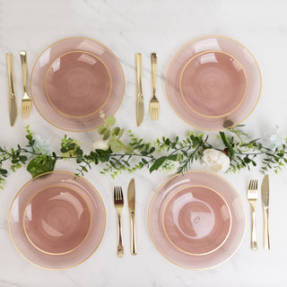 Elegant pink dinner plates set with gold trim and cutlery on a marble table.