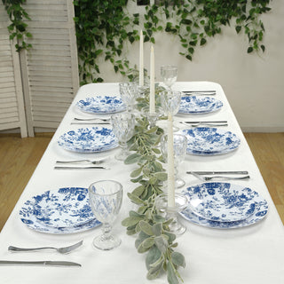 Elegant blue and white dinnerware set on a table with candles and greenery.