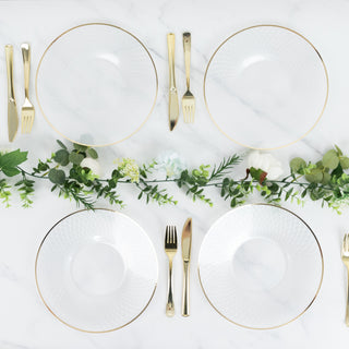 Elegant set of four clear plates with gold rims and greenery on a marble table.