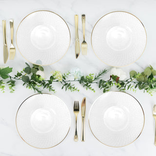 Elegant white plates with gold trim arranged with cutlery and greenery.