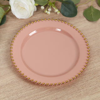 Pink plate with gold beaded rim on a textured surface.