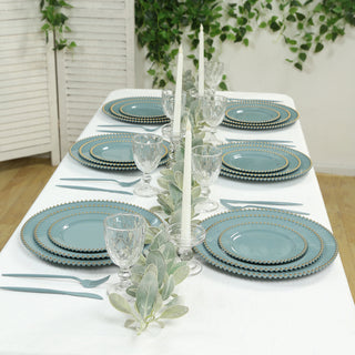 Elegant dining table set with turquoise plates and glassware, adorned with greenery.