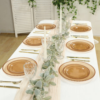 Elegant table setting with amber plates, glassware, and greenery decor.