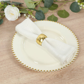 Elegant white napkin with gold ring on decorative plate surrounded by greenery.