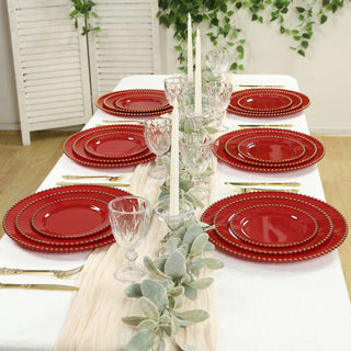 Elegant red dinner plates set on a beautifully arranged table with candles and greenery.