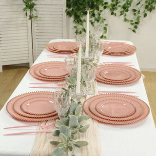 Elegant pink dinnerware set arranged on a table with greenery and candles.
