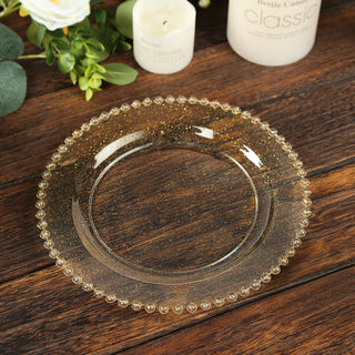 Gold beaded glass plate on a wooden table with candles and greenery.
