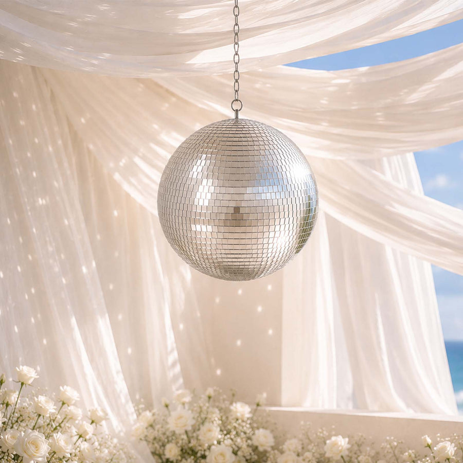 Silver disco ball hanging under sheer drapes with white floral decor and ocean view