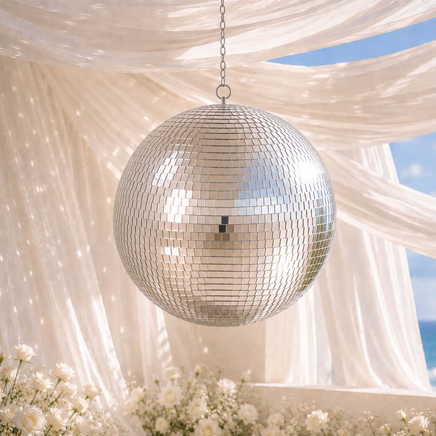 Silver disco ball hanging under draped fabric with white flowers and blue sky