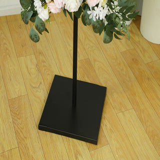 Black metal base of a floral stand with faux flowers arranged above.