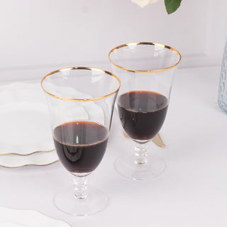 Elegant glass wine goblets with gold rim, filled with red wine.