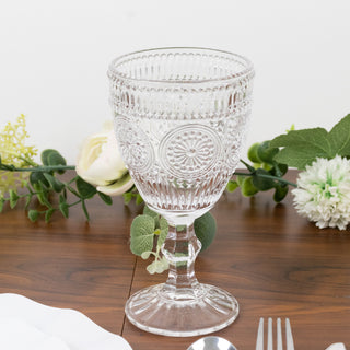 Clear vintage-style glass goblet on a wooden table surrounded by greenery.