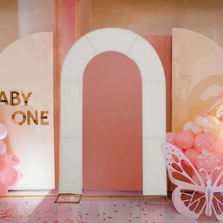 White arch decoration for events with pink backdrop and balloons.