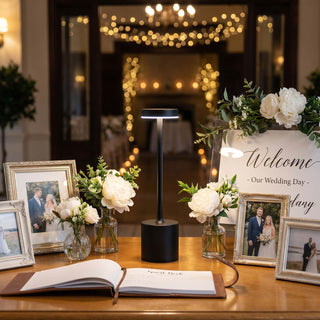 Wedding guest book table with flowers, framed photos, welcome sign, and table lamp