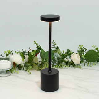 Black modern cordless LED table lamp on marble surface with greenery decor