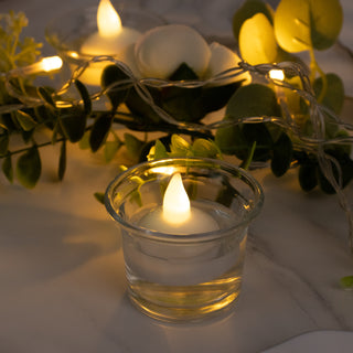 LED candle in a glass holder surrounded by greenery and fairy lights.