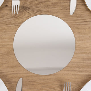 Round silver mirror placemat on a wooden table with cutlery.