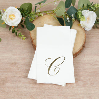 Personalized gold initial napkins on a wooden slice with greenery and flowers.