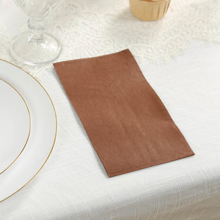 Brown napkin on a textured tablecloth next to elegant dinnerware.