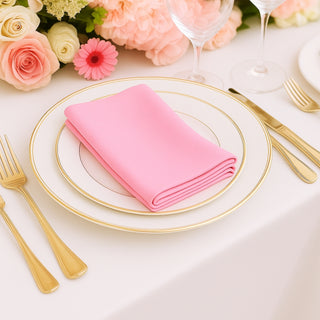 Pink napkin elegantly folded on a gold-rimmed plate, surrounded by floral decor.