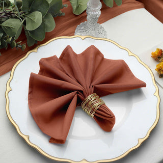 Rust-colored napkin elegantly folded on a decorative plate with a gold rim.