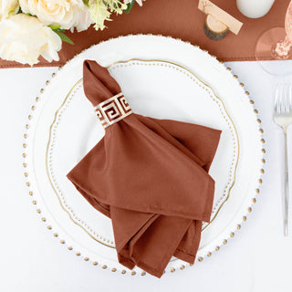 Brown napkin with decorative band on a dinner plate with floral centerpiece.