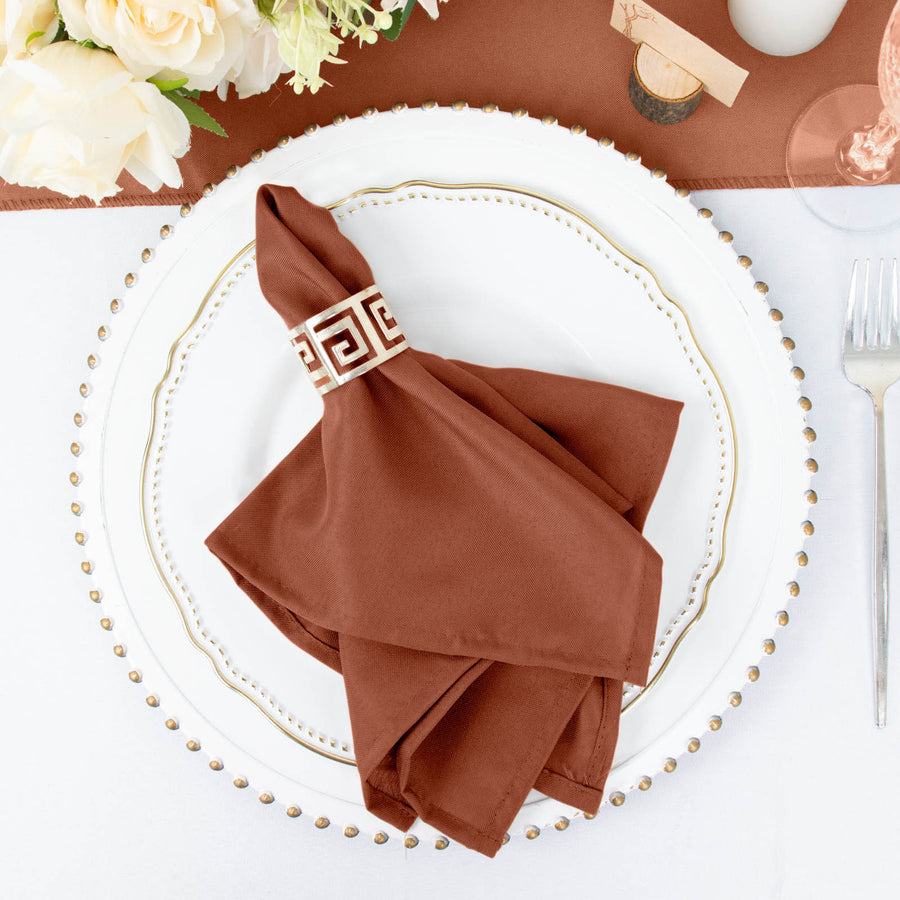 Brown napkin with decorative band on a dinner plate with floral centerpiece.
