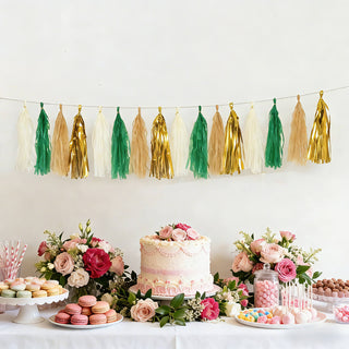 Colorful tassel garland above a beautifully decorated dessert table with flowers and cake.