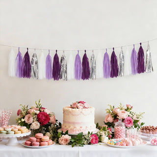 Colorful tassel garland above a decorated dessert table with flowers and cakes.