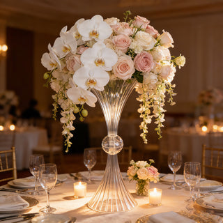 Elegant floral centerpiece with orchids and roses in a clear vase at a banquet table.