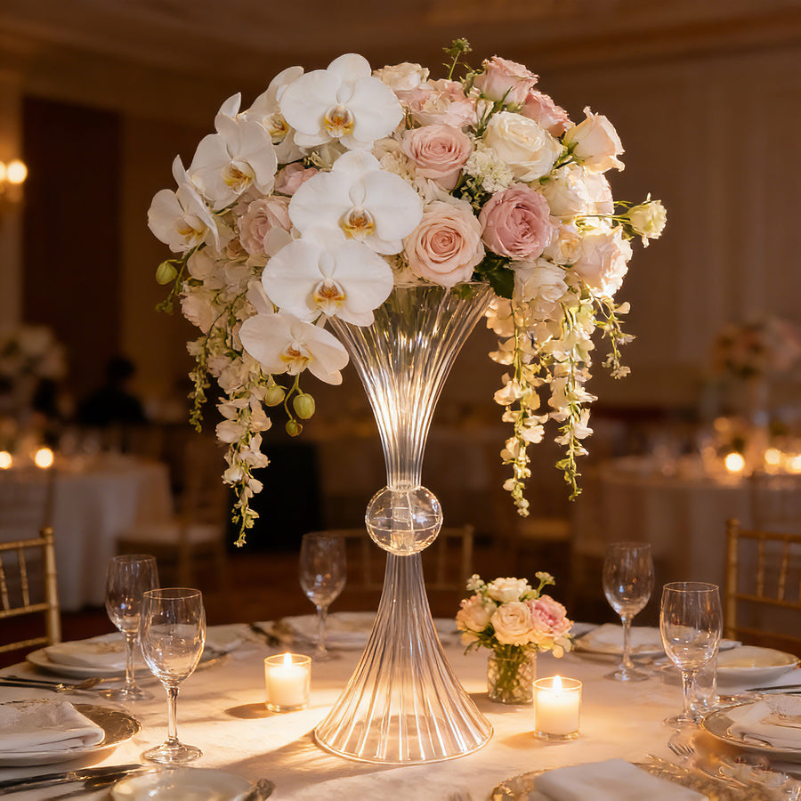 Elegant floral centerpiece with orchids and roses in a clear vase at a banquet table.