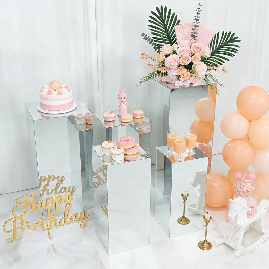 Birthday celebration setup with mirrored pedestals, cakes, flowers, and balloons.